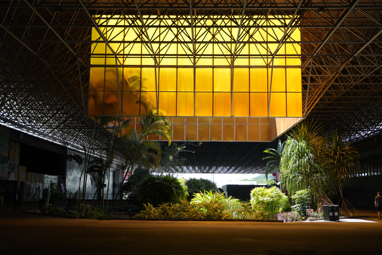 A luminous yellow pavilion suspended beneath a steel roof above tropical plants.