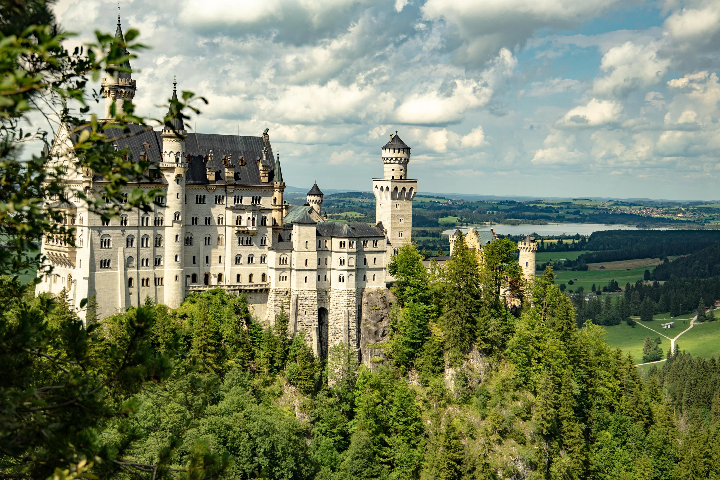 Neuschwanstein Castle rising above forested Bavarian hills beneath summer clouds.