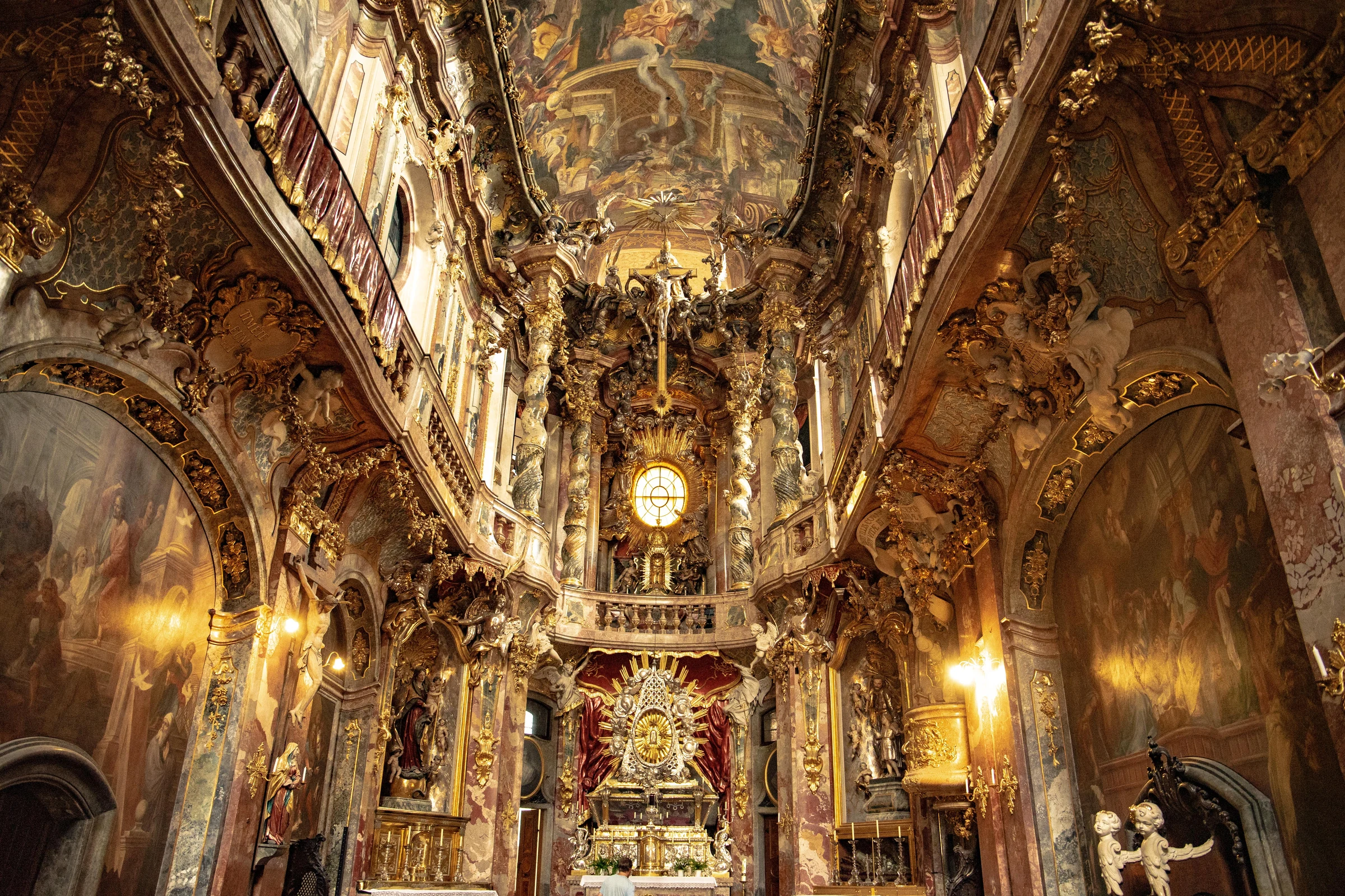 An ornate Baroque church interior covered in gilded sculpture, frescoes, and warm light.