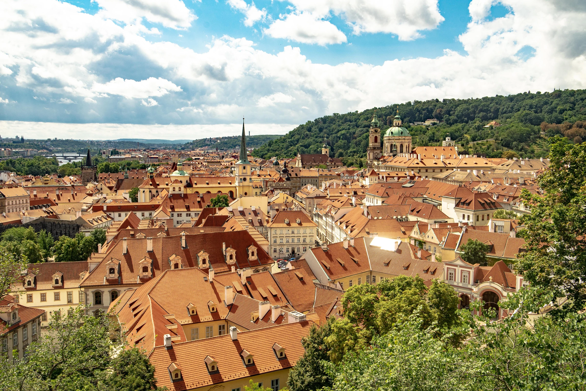 Red roofs and church domes spreading across Prague beneath a bright summer sky.