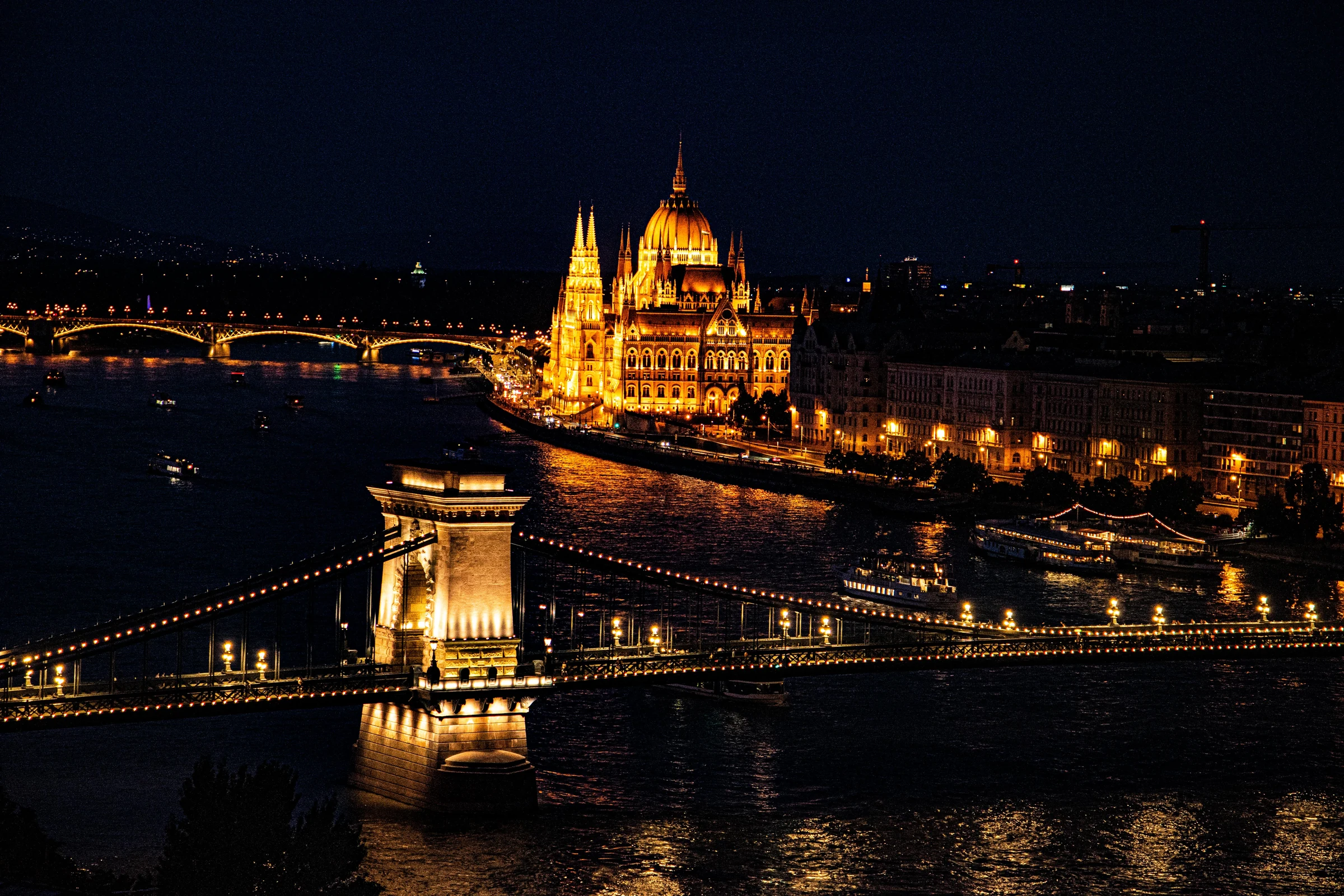 The Hungarian Parliament glowing across the Danube beyond the Szechenyi Chain Bridge at night.