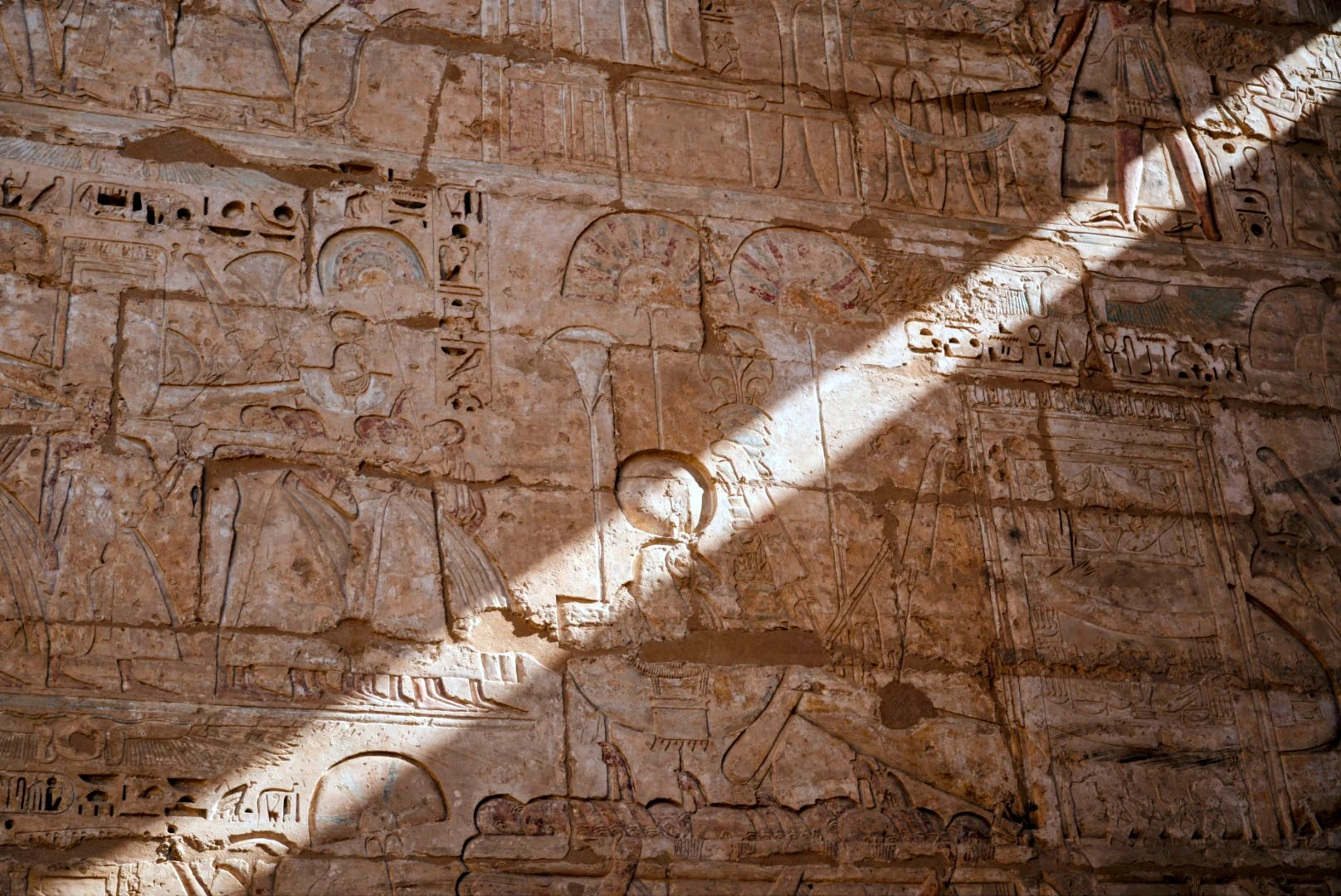 Ancient Egyptian wall reliefs crossed by a shaft of sunlight.