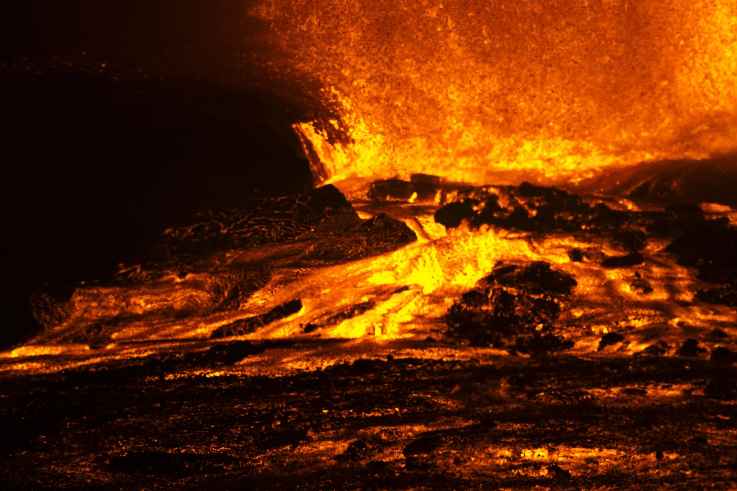 A glowing lava channel flowing below an eruption.