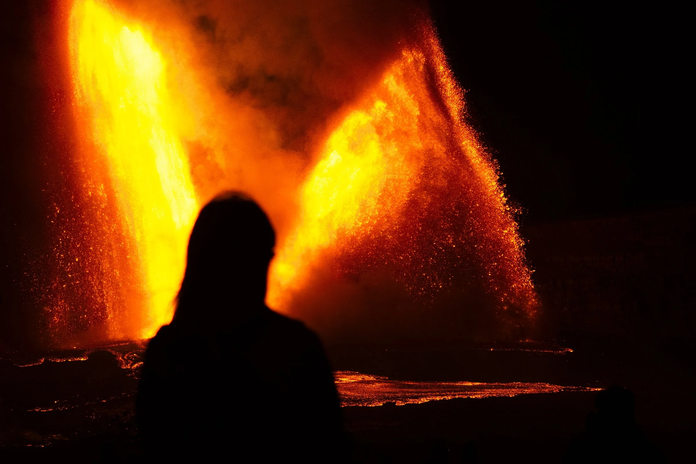 A silhouetted observer watching twin lava fountains.