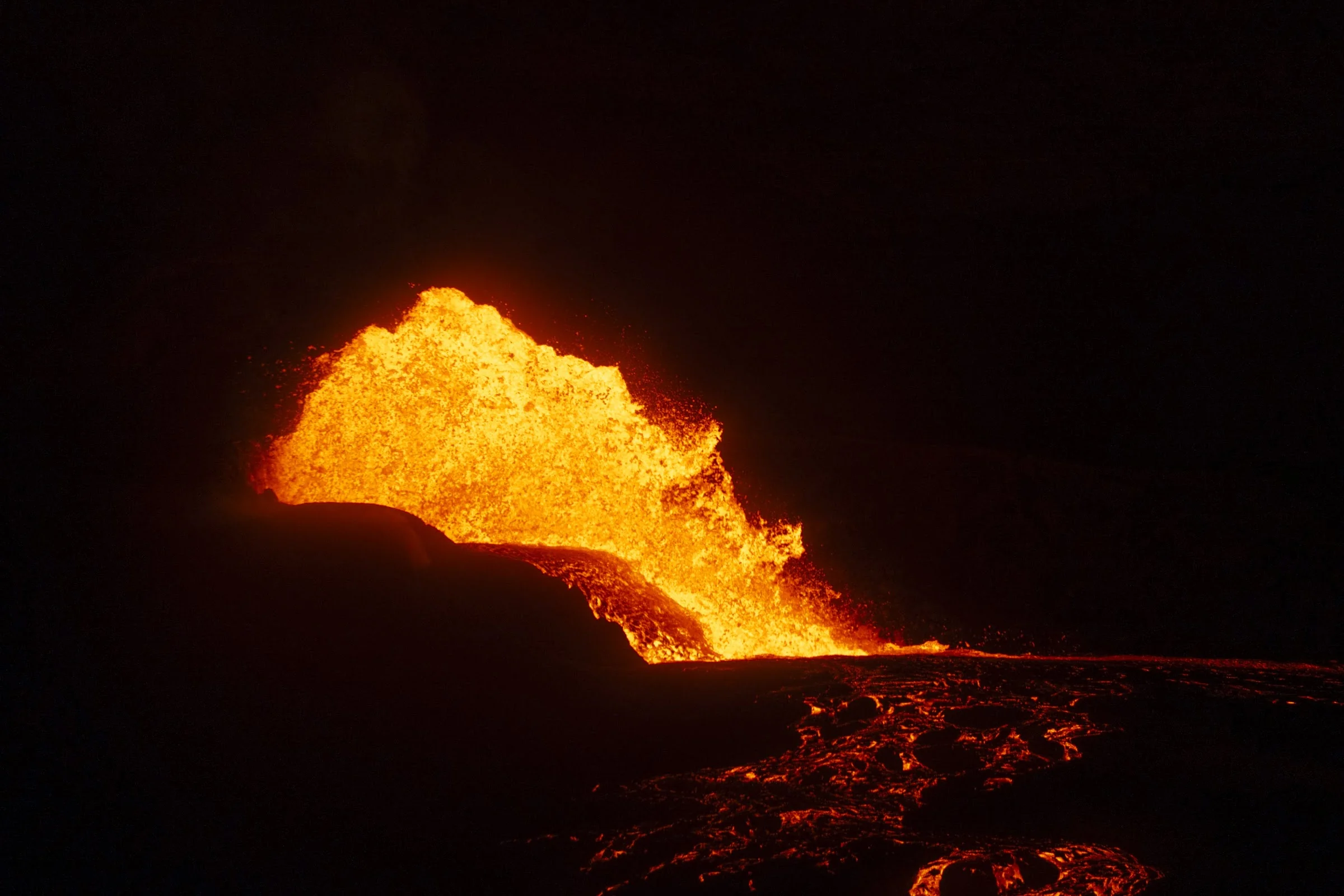 A distant lava fountain glowing above a dark ridge.