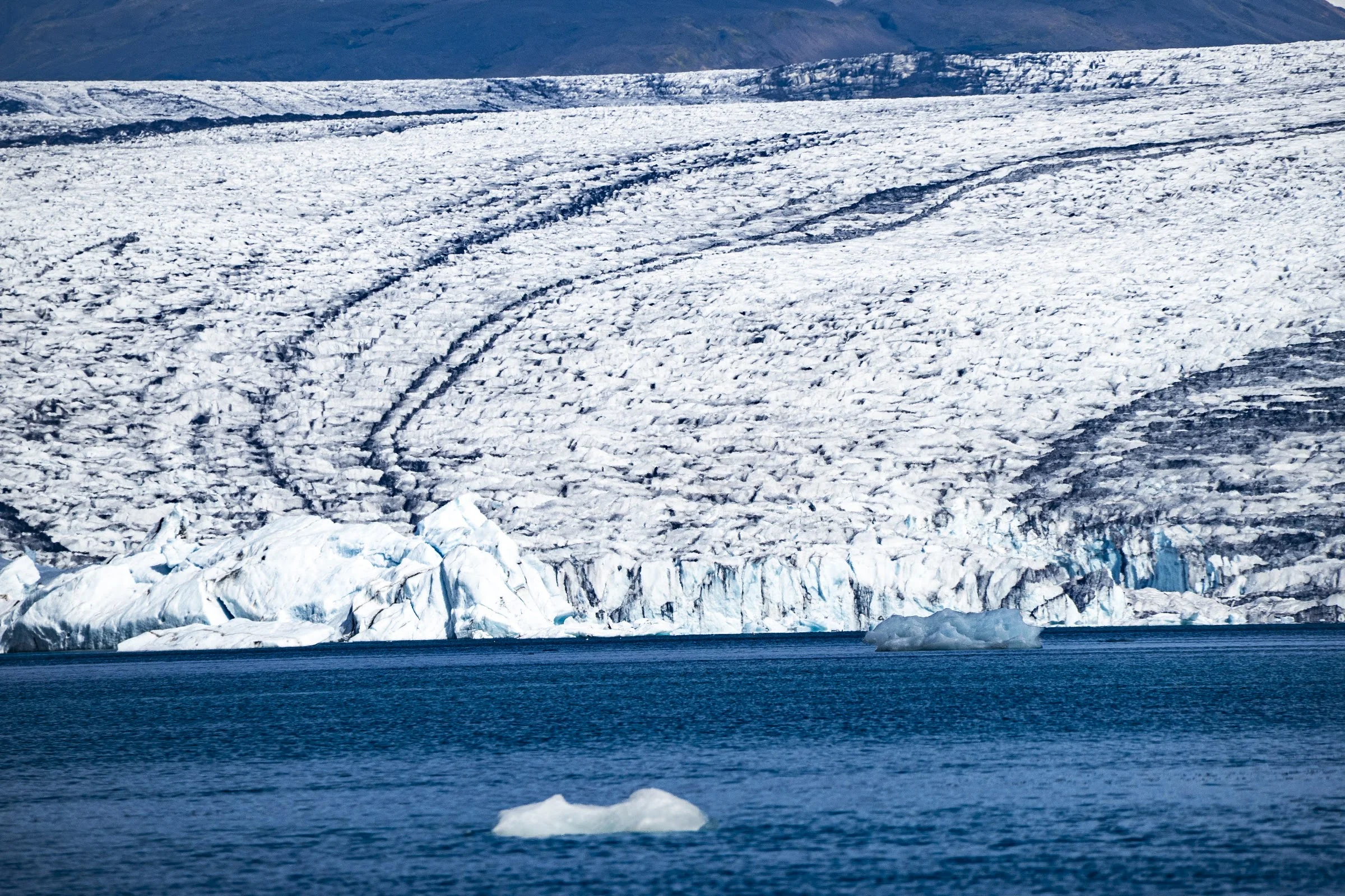 A glacier terminus descending toward a still lagoon.