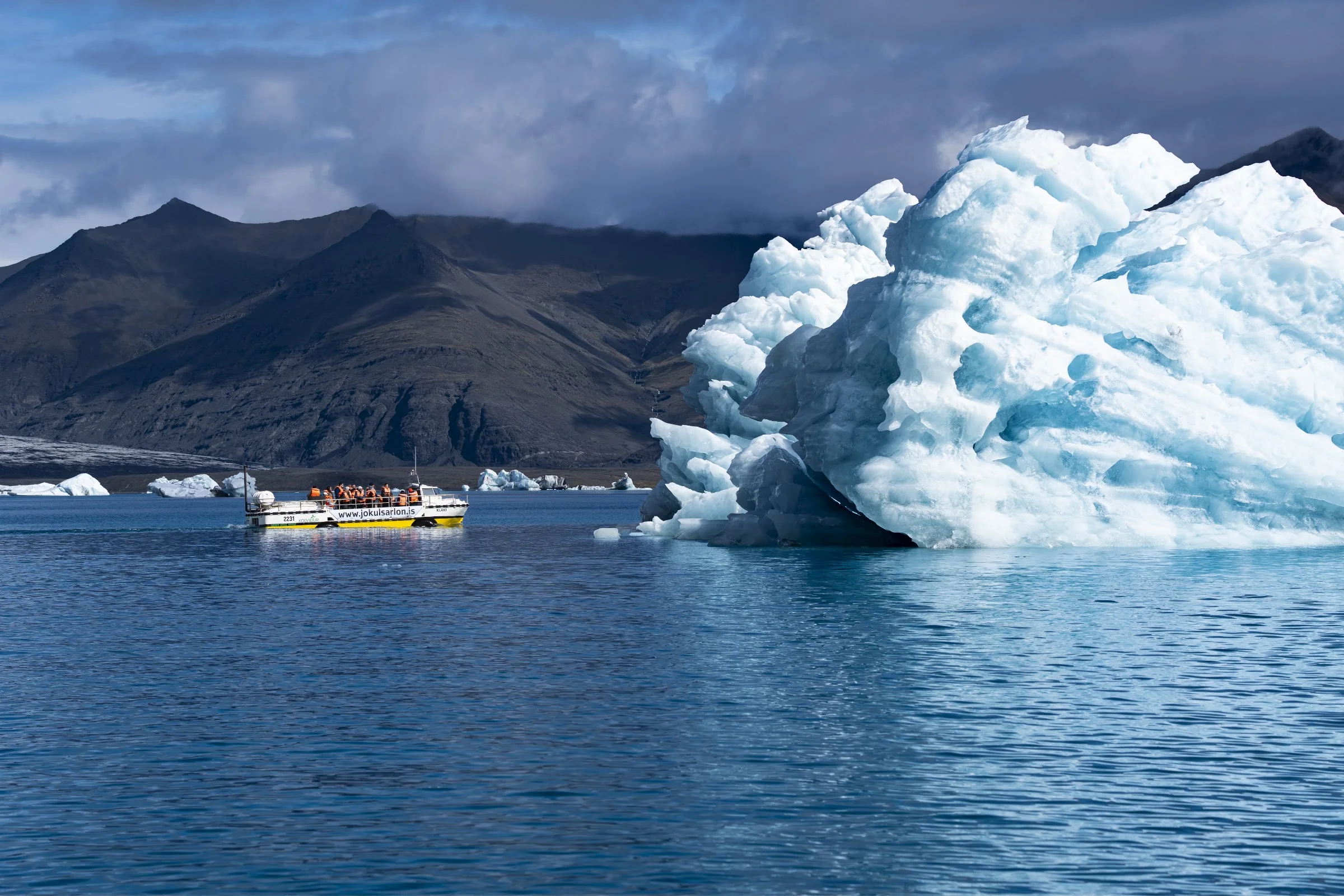 A blue iceberg rising beside a small yellow boat.