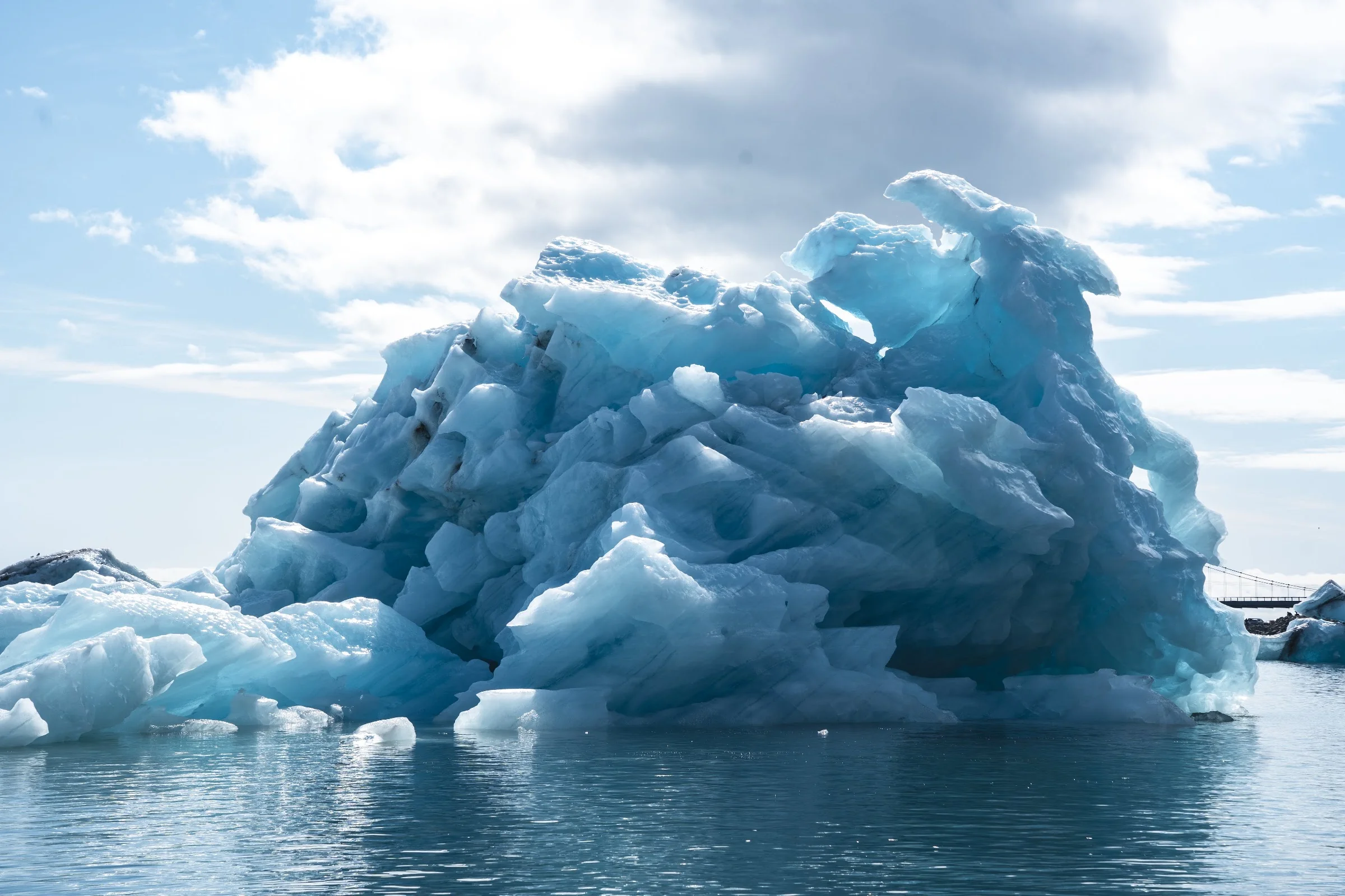A sculptural blue iceberg beneath bright clouds.