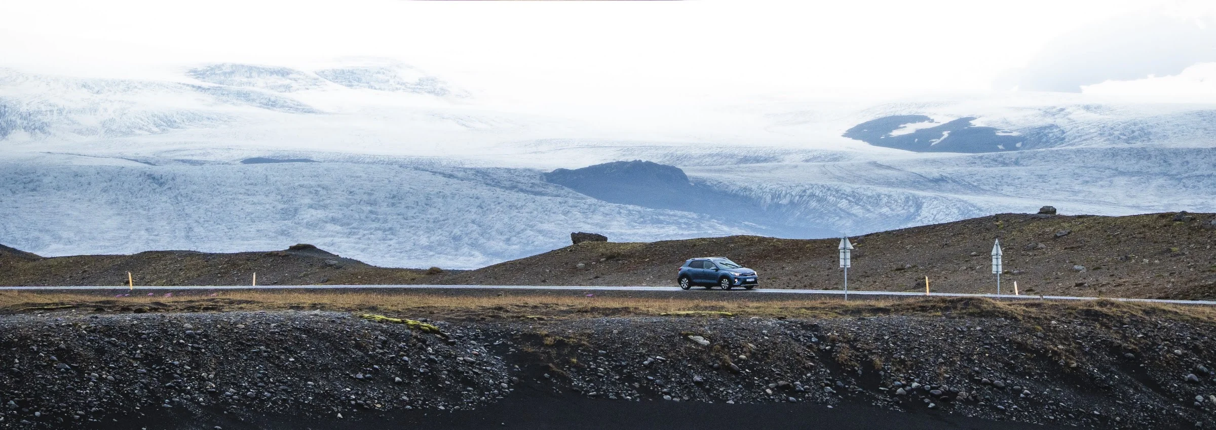 A car and lone figure on a road beneath an immense glacier.