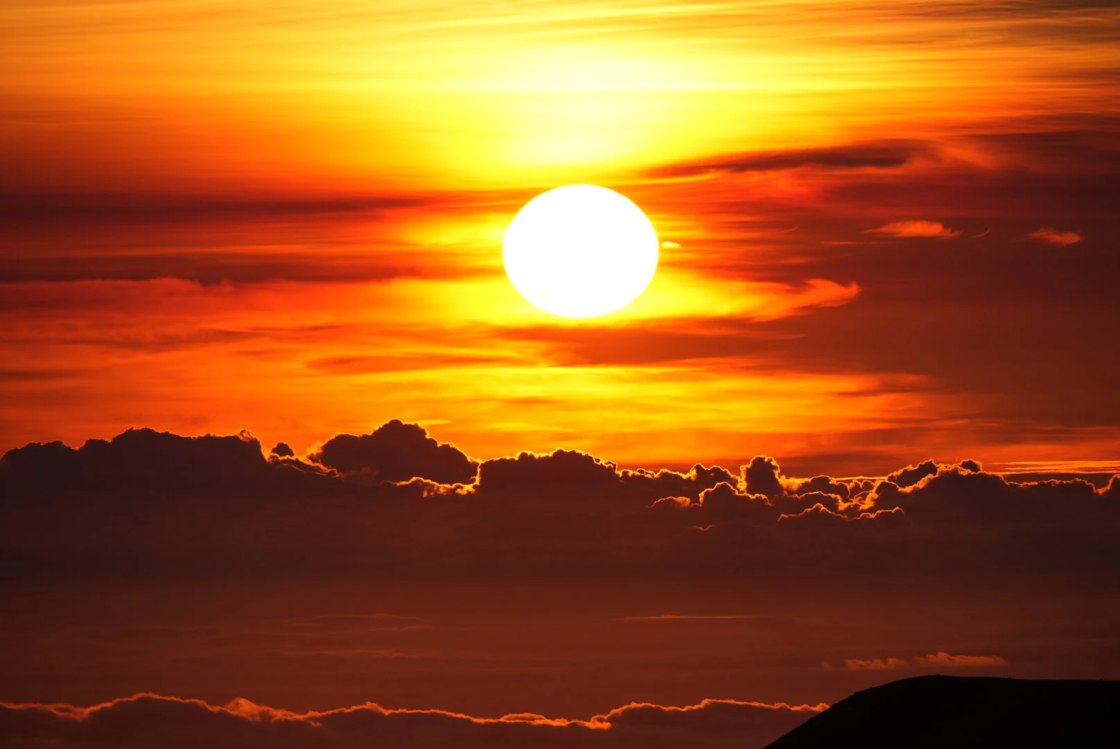 The sun glowing white above layered orange clouds at sunset.