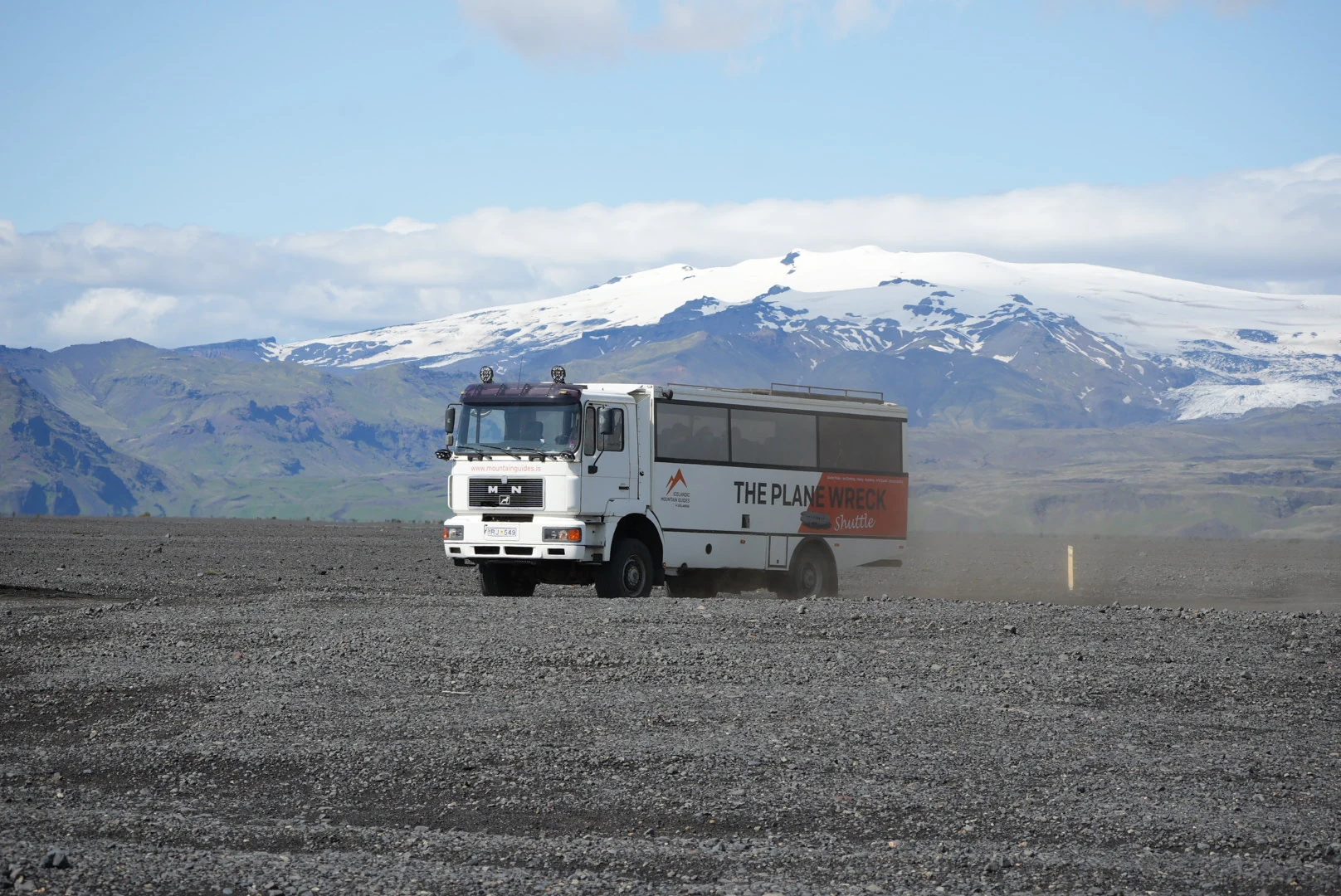 A plane-wreck shuttle crossing black sand beneath an Icelandic glacier.