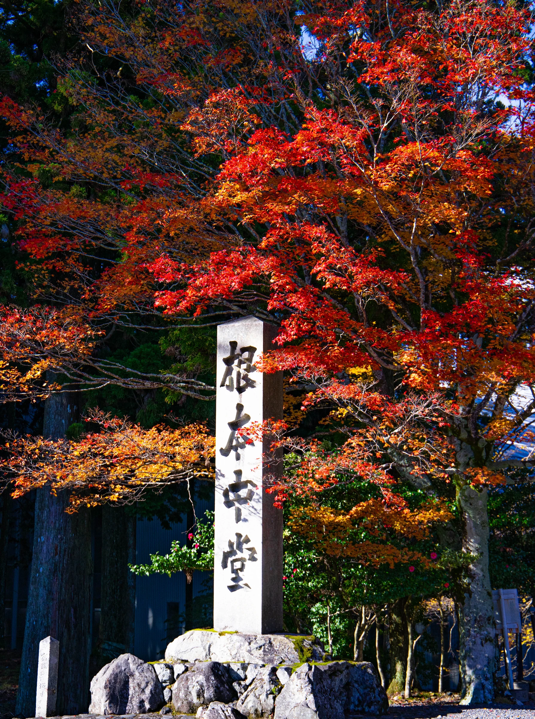 A stone temple marker framed by vivid red and orange autumn foliage.