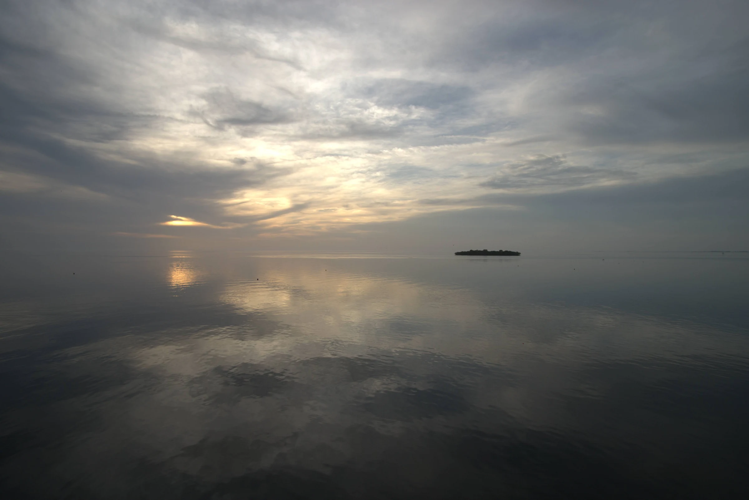 A small island and clouded sunset reflected across still water.