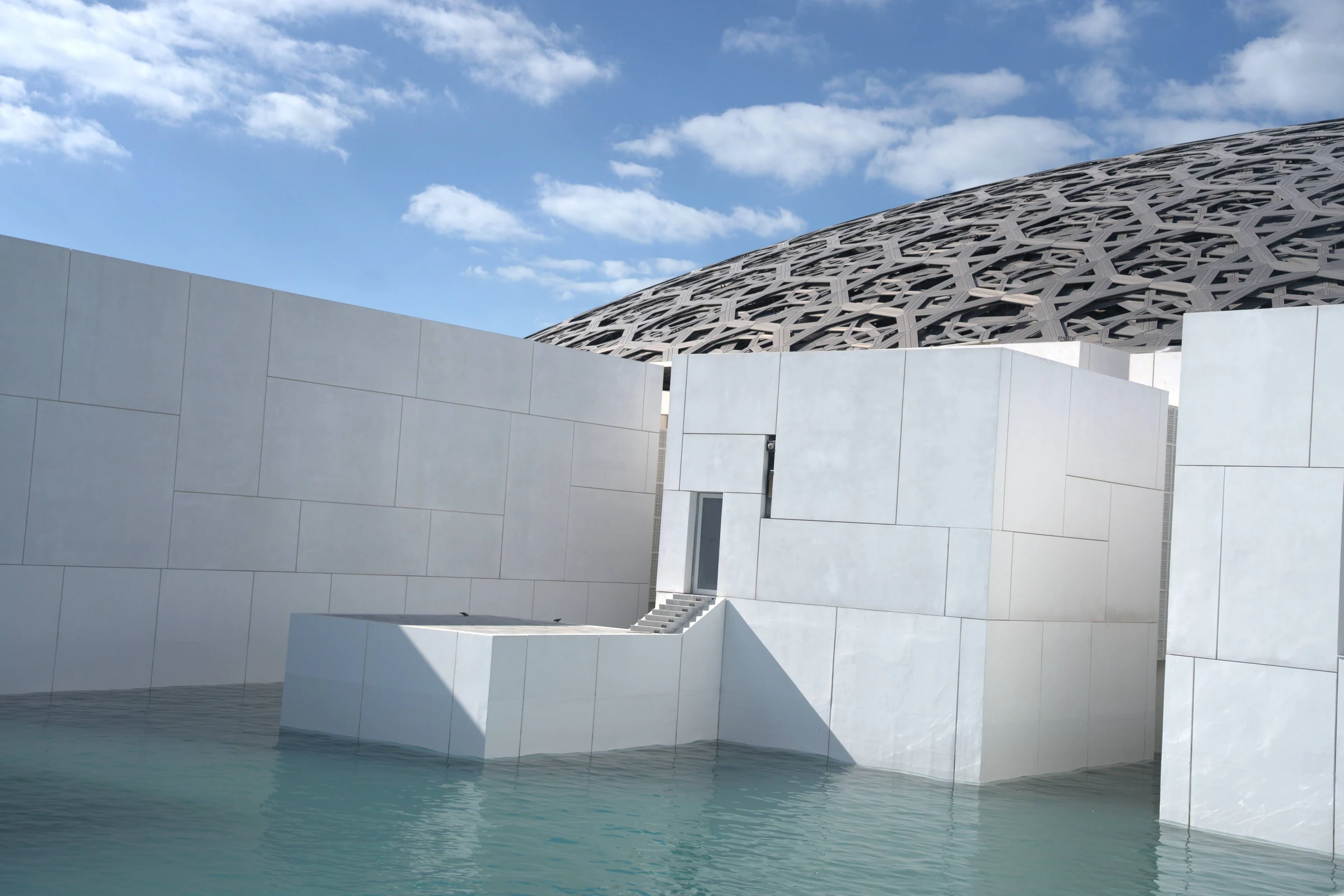 The geometric dome and white waterfront galleries of Louvre Abu Dhabi.