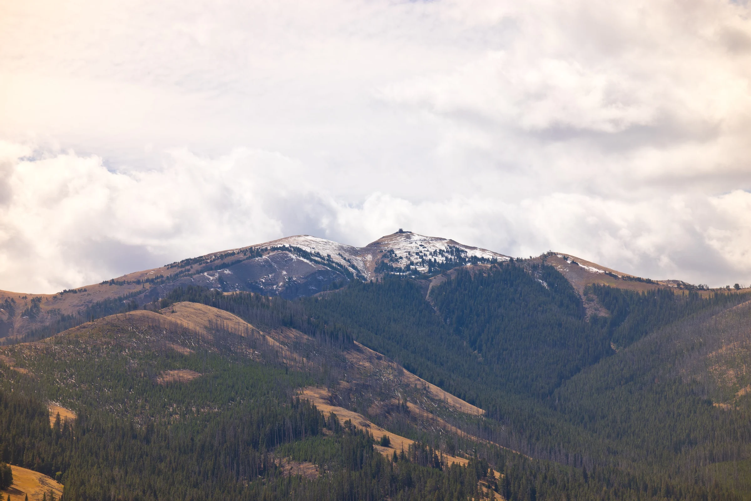 Autumn-tinted ridges and a snow-dusted mountain beneath layered clouds.